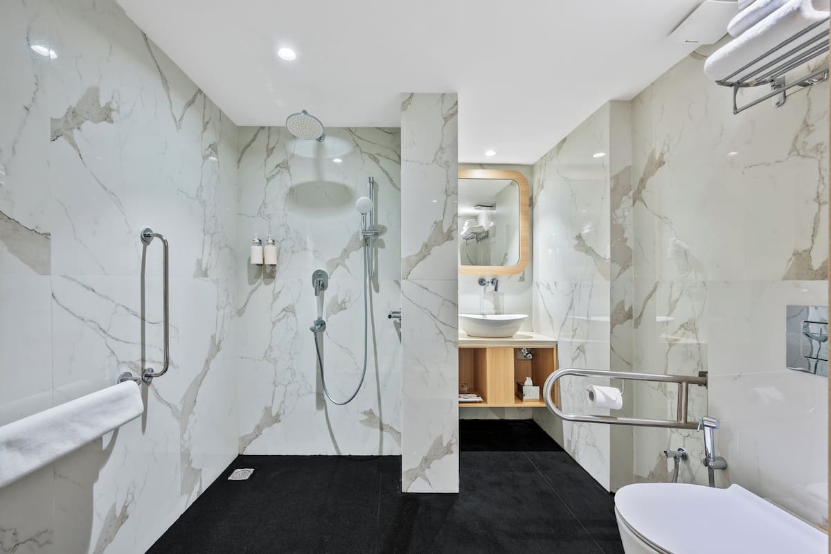 A modern bathroom with marble walls, a black floor, a white bathtub, and a shower area.