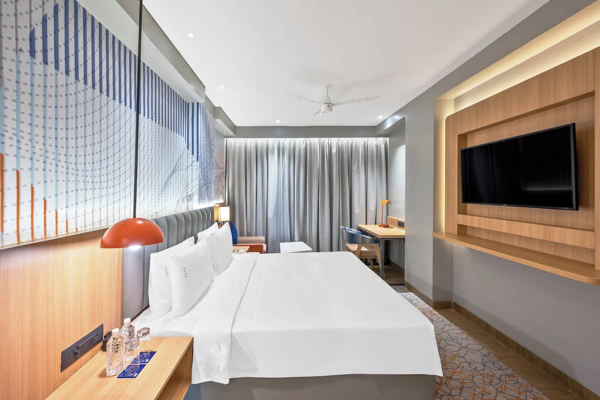 A hotel room with a bed, a desk, a TV, a ceiling fan, and a patterned wall.