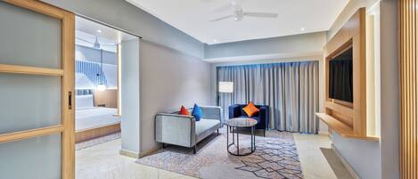 A modern hotel room with a bed, a sofa, a small table, a TV, and a ceiling fan.