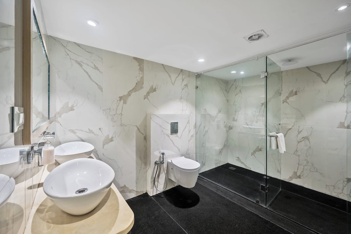 A modern bathroom with a marble wall, a glass shower enclosure, and a sink with a beige countertop.