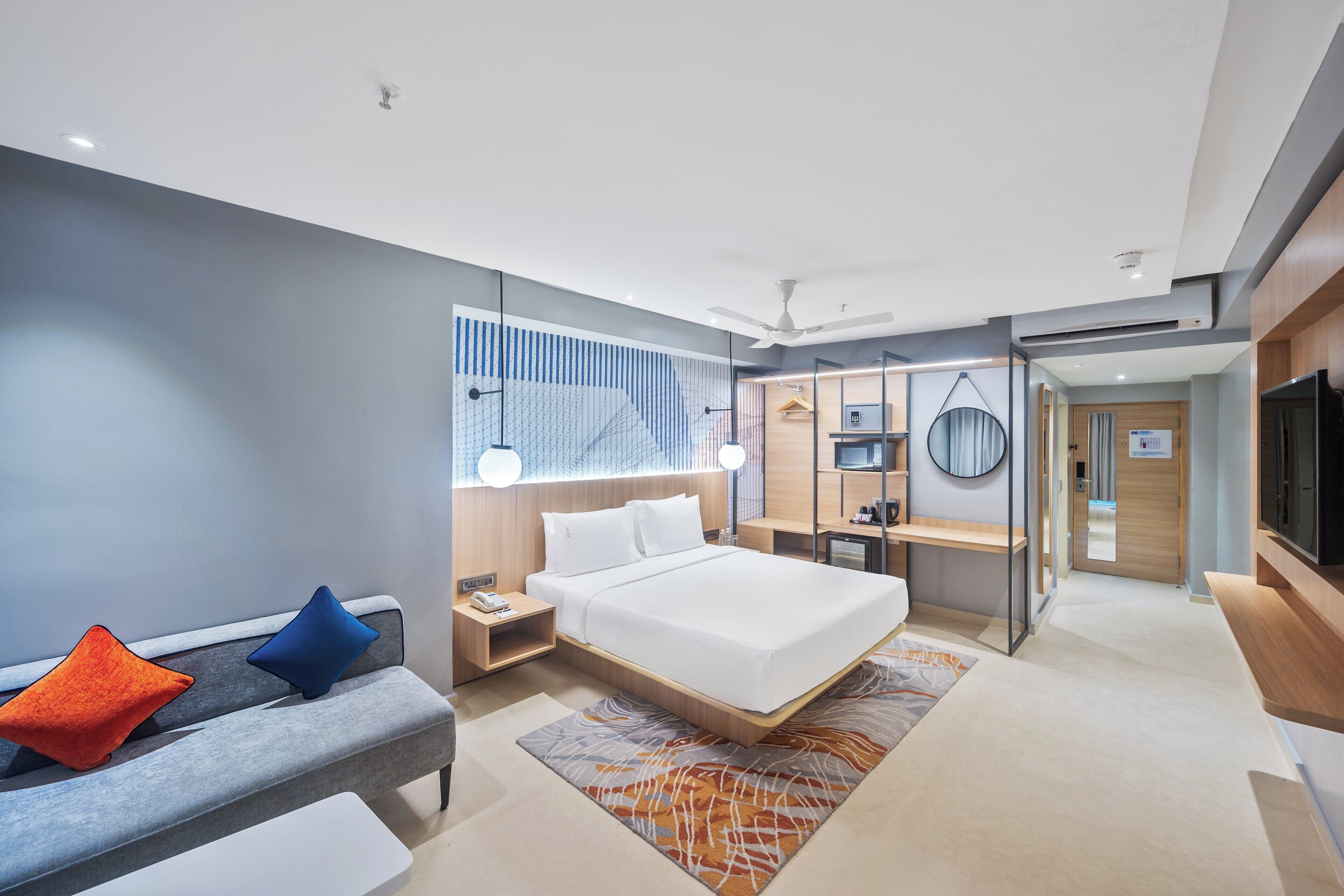 A modern hotel room with a large bed, a sofa, a desk, and a TV.