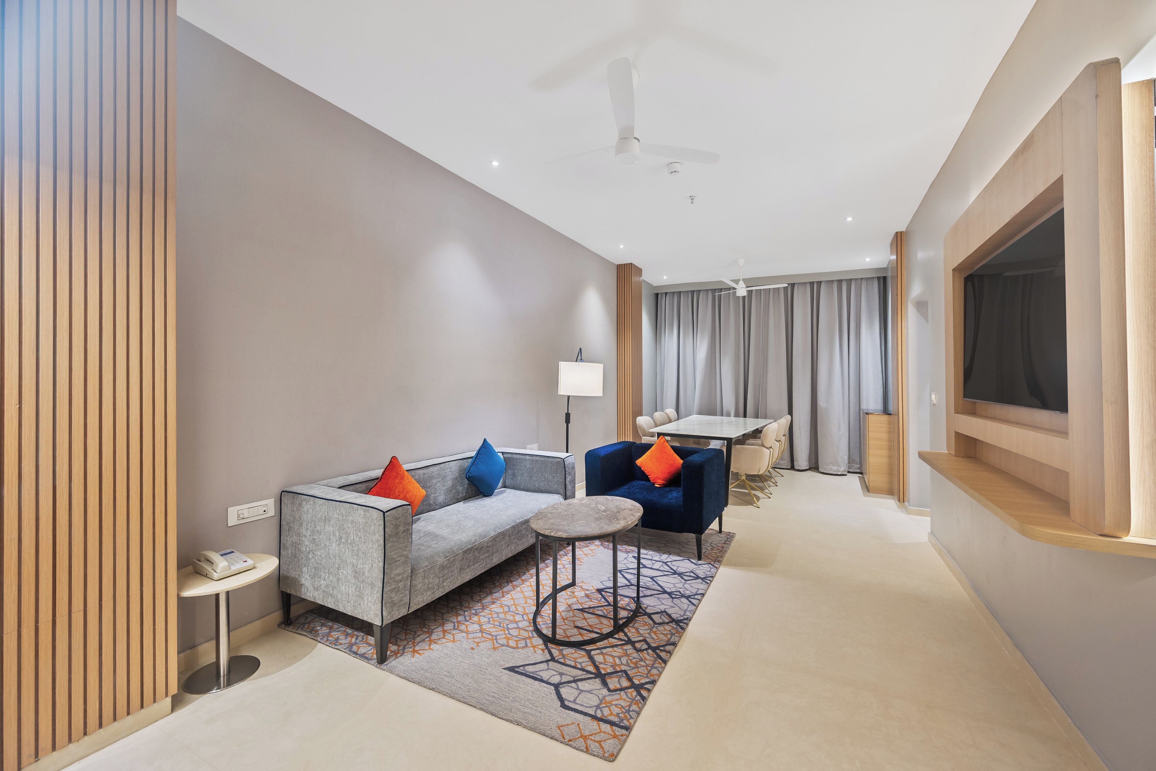 A modern hotel room with a sofa, armchair, round table, and a TV.