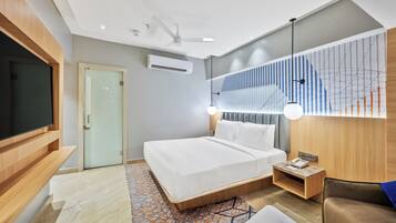 A modern hotel room with a bed, a TV, a desk, and a wall-mounted light fixture.