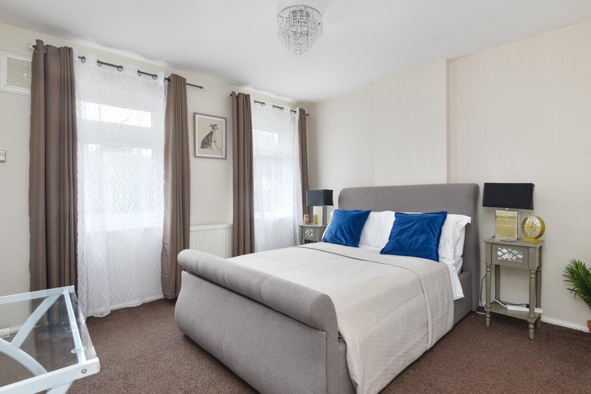 A bedroom with a bed, curtains, a bedside table with a lamp, a clock, and a small plant.