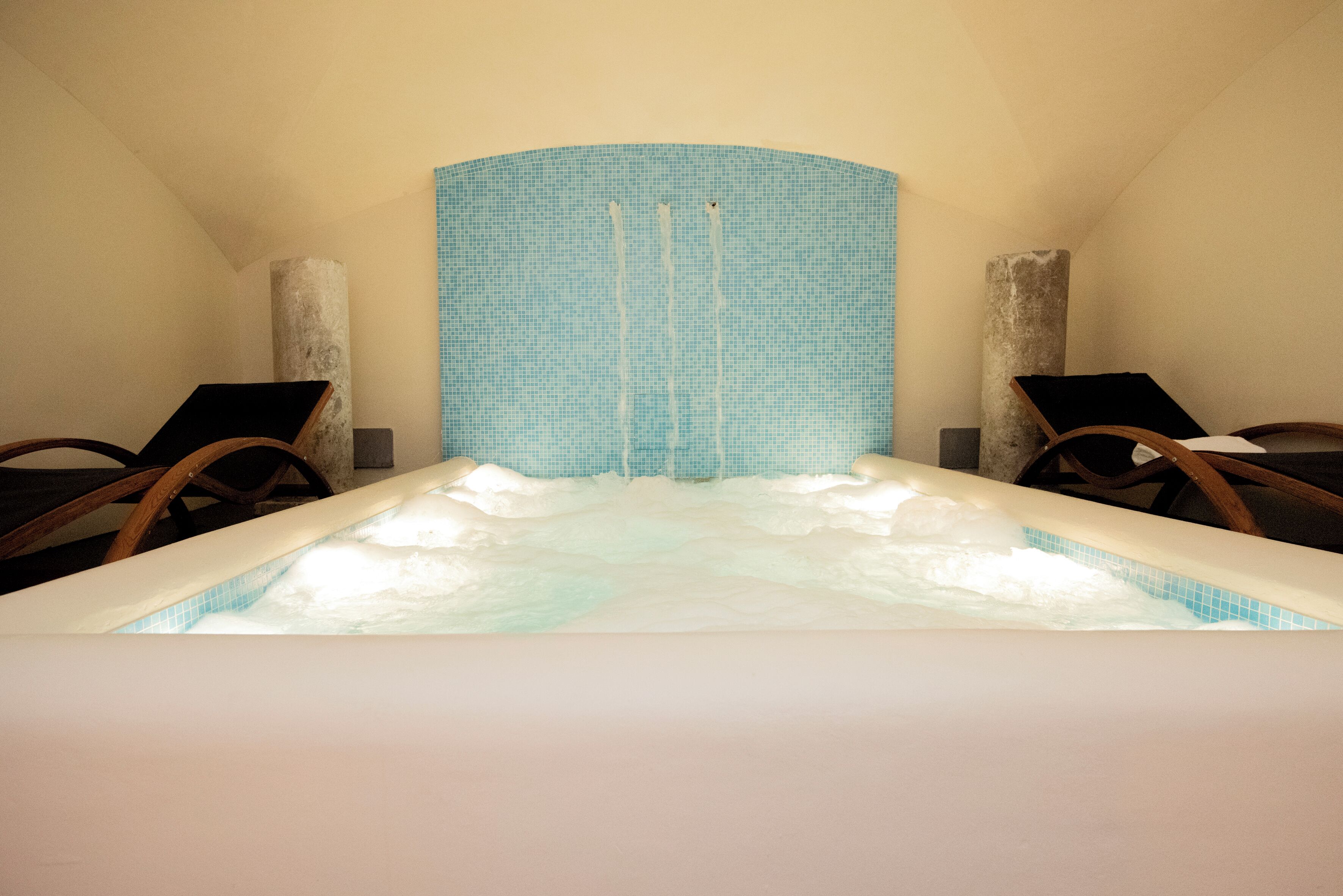 Une pièce avec une grande baignoire, deux chaises en bois et un mur à texture.