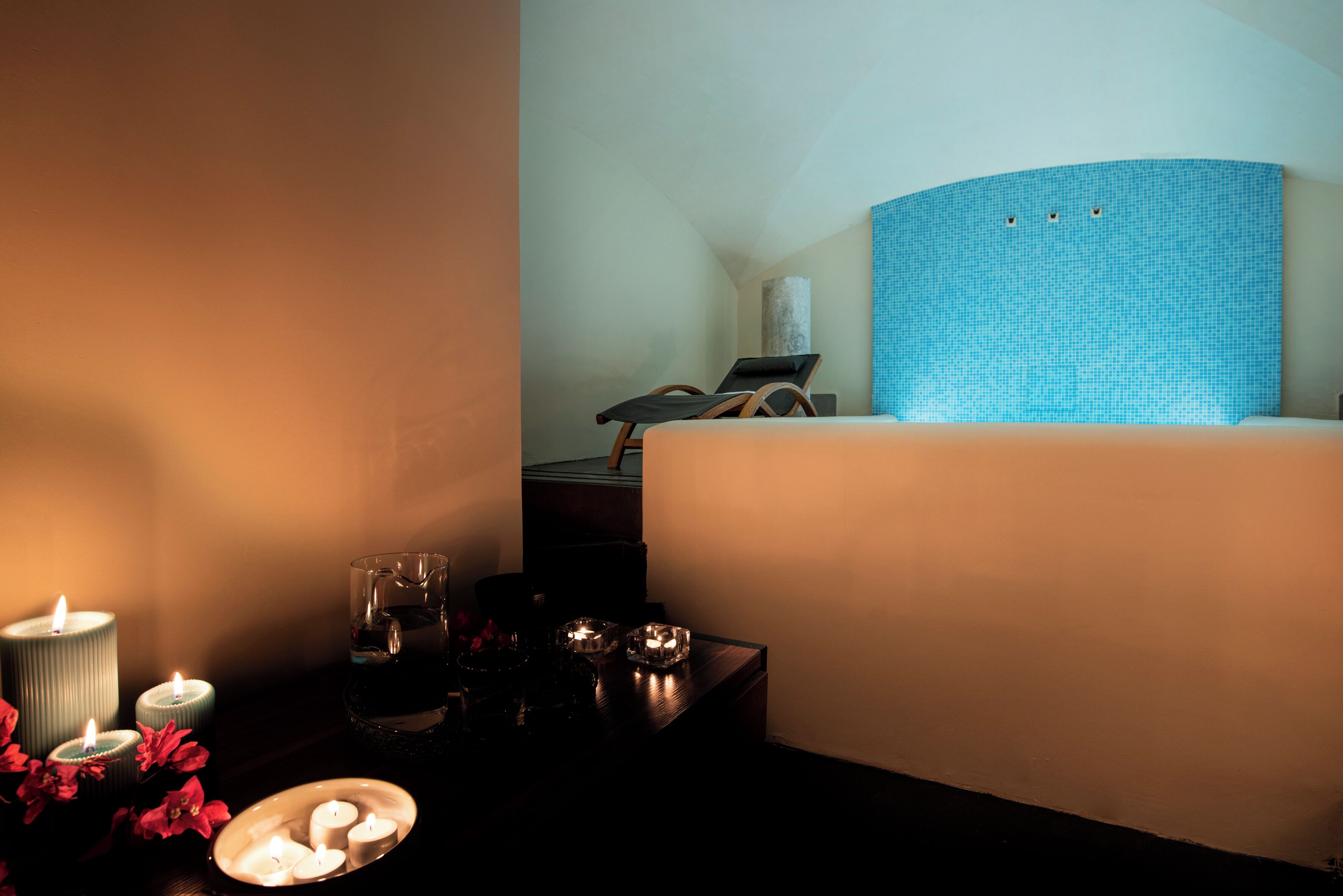Quarto de hotel com cama, mesa de cabeceira com velas, um copo de água e uma pequena tigela decorativa.