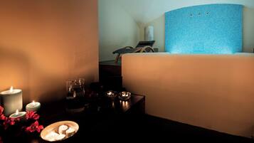 Quarto de hotel com cama, mesa de cabeceira com velas, um copo de água e uma pequena tigela decorativa.