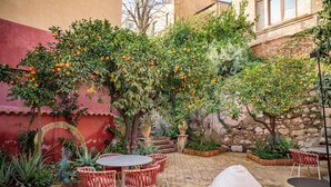 An outdoor patio with a brick floor, red and white walls, and orange trees. There are round tables and chairs, and a sofa. - Villa Conrad by Hotel Metropole Taormina (Taormina)
