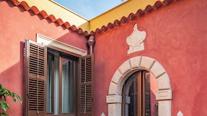 A red building with a wooden door and window shutters, a stone staircase, and a potted plant. - Villa Conrad by Hotel Metropole Taormina (Taormina)