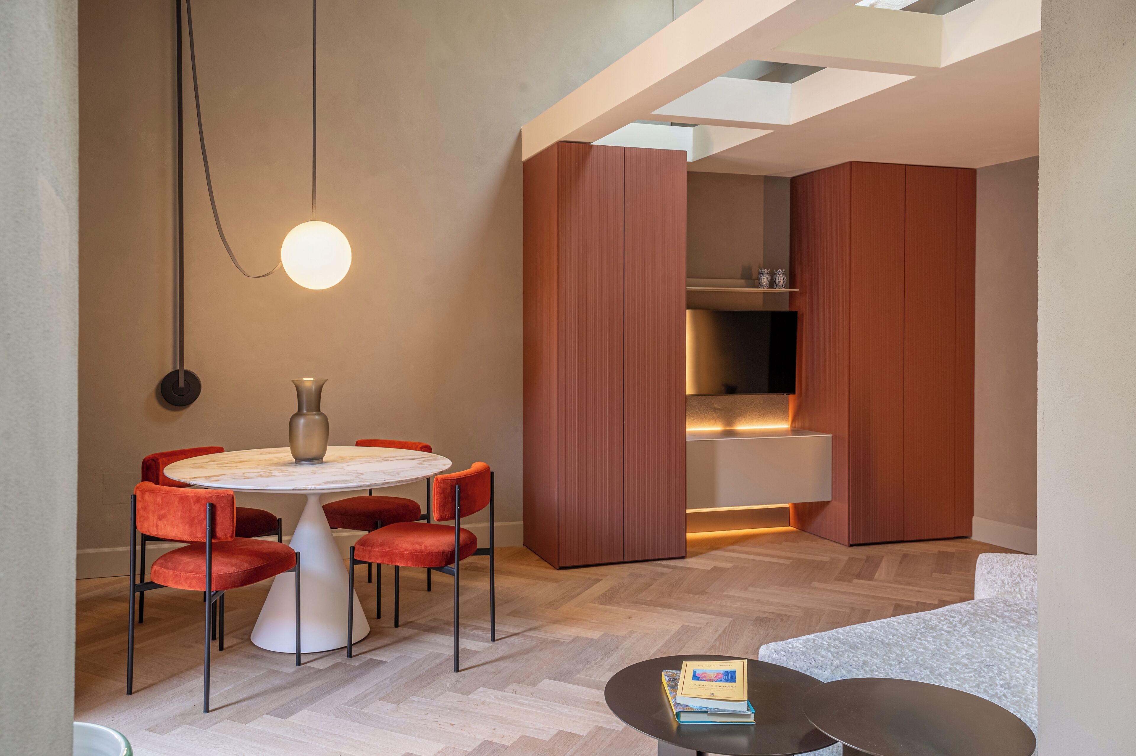 Un área de comedor moderna con una mesa redonda, sillas rojas y una lámpara colgante.