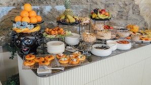 A buffet with various food items, including fruits, pastries, and a decorative face sculpture. - Villa Conrad by Hotel Metropole Taormina (Taormina)