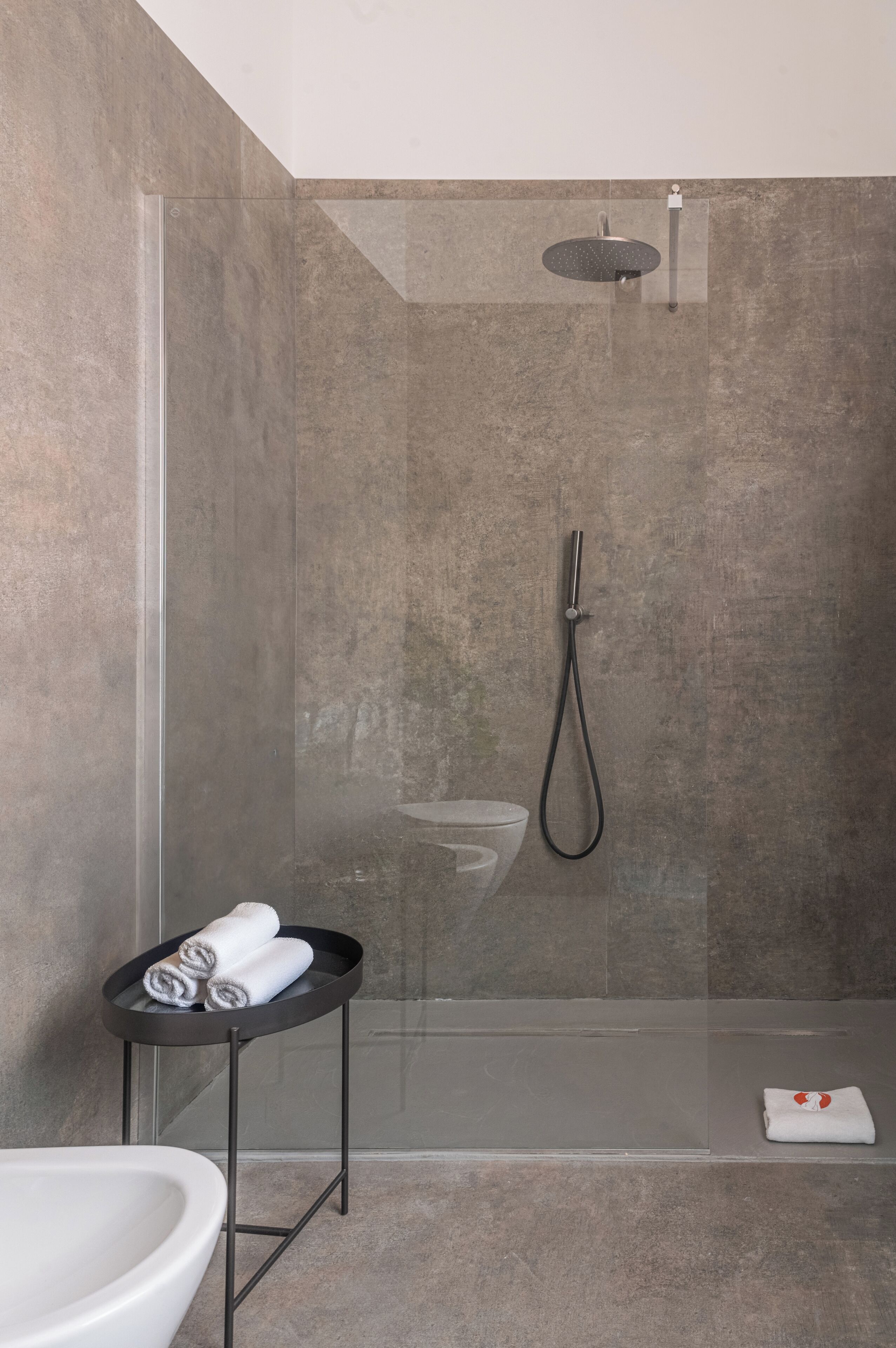 A modern bathroom with a glass-enclosed shower, a white sink, and a small table with towels.