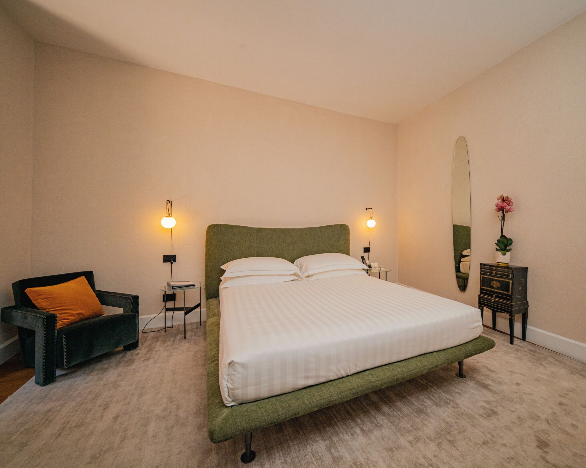 Un dormitorio con una cama individual, dos lámparas de noche, una silla, una mesita, un espejo y un aparador.