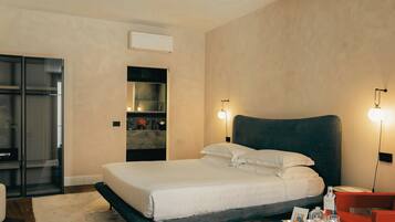 A modern hotel room with a large bed, a built-in vanity, a seating area with a red chair, and a small table with amenities.