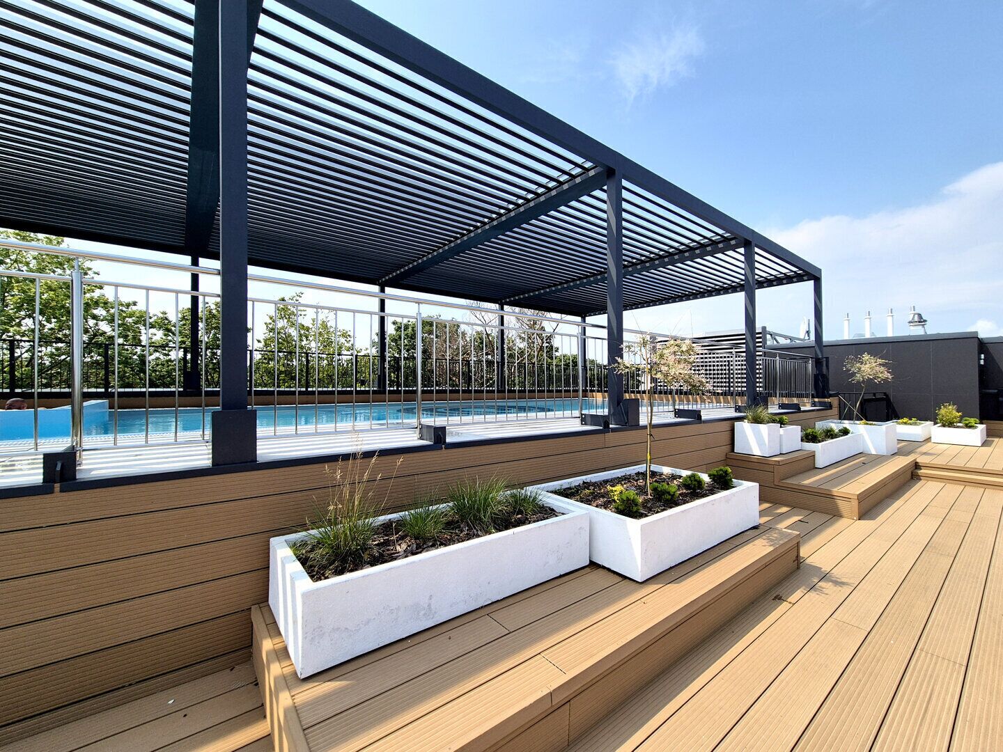 A rooftop pool area with a covered seating area and planters.