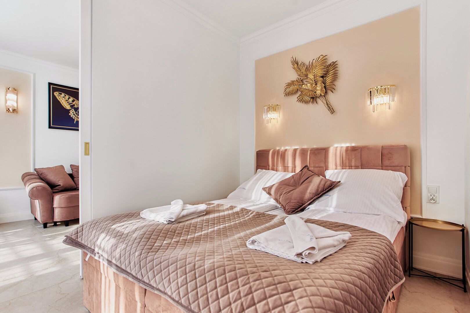 A modern bedroom with a large bed, a chaise lounge, and decorative wall sconces.
