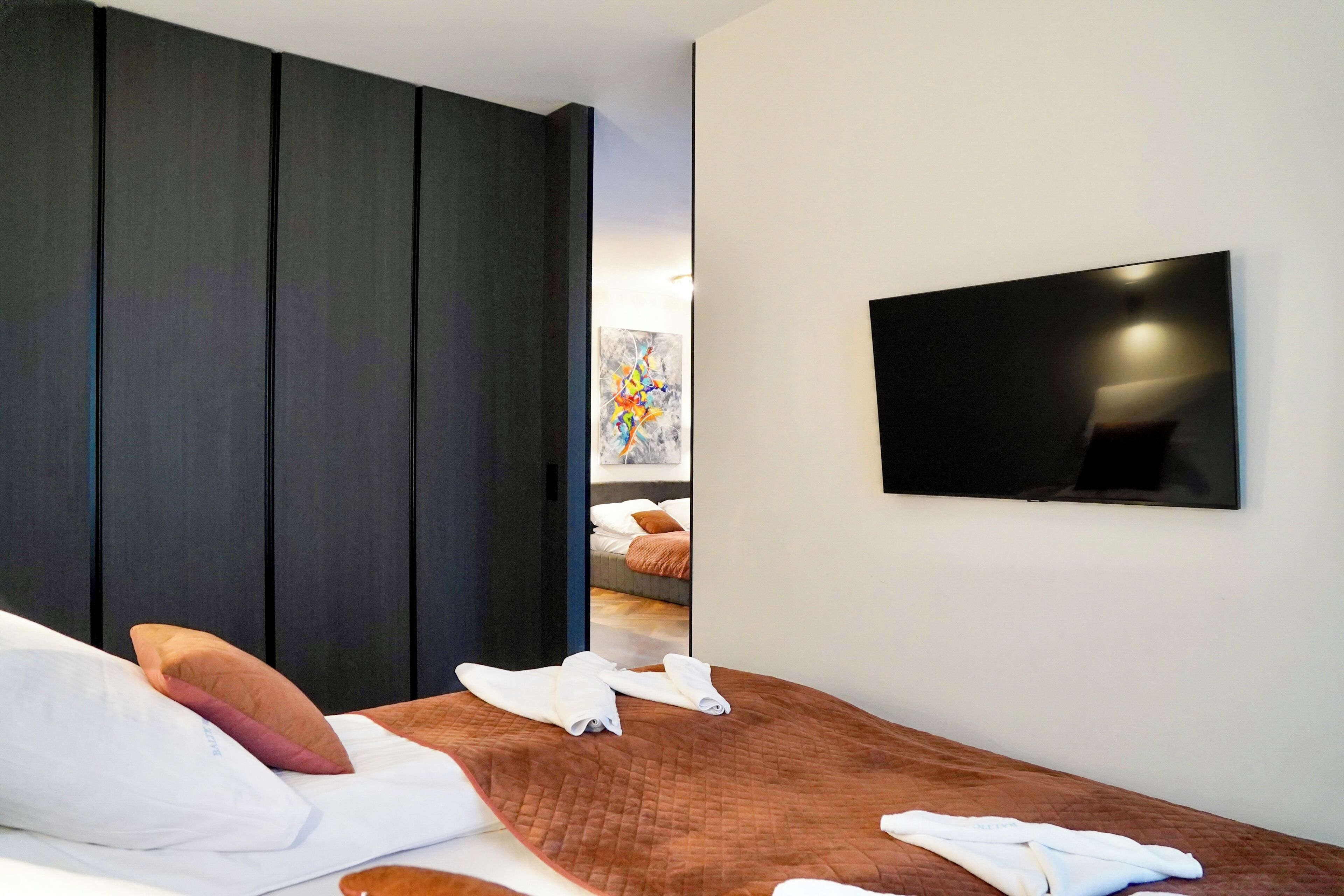 Ein modernes Hotelzimmer mit einem großen Bett, einem an der Wand befestigten Flachbildfernseher und einem großen Spiegel, der das Zimmer widerspiegelt.