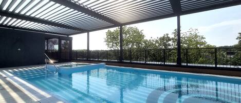 An indoor swimming pool with a clear view of the surrounding trees and a covered area with a metal roof.