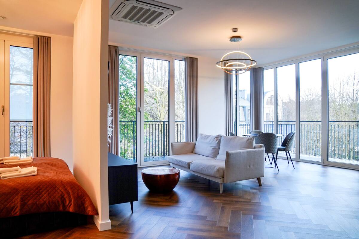 Ein modernes Hotelzimmer mit einem großen Bett, einer Couch, einem Couchtisch und einem Balkon mit Blick ins Freie.