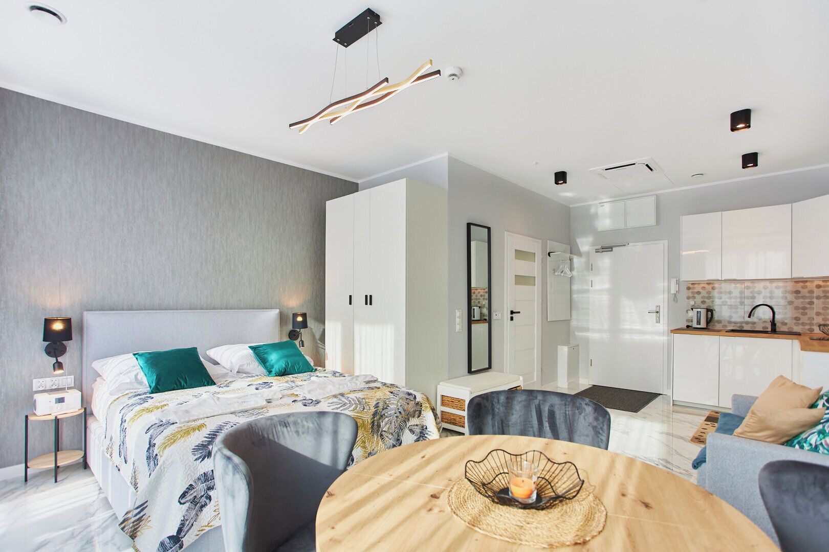 Ett modernt hotellrum med en säng, ett nattduksbord, en lampa och utsikt över köksdelen.