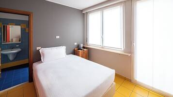 Une chambre d’hôtel comprenant un lit, une table de chevet, une commode, une fenêtre et une salle de bain avec un lavabo et un miroir.