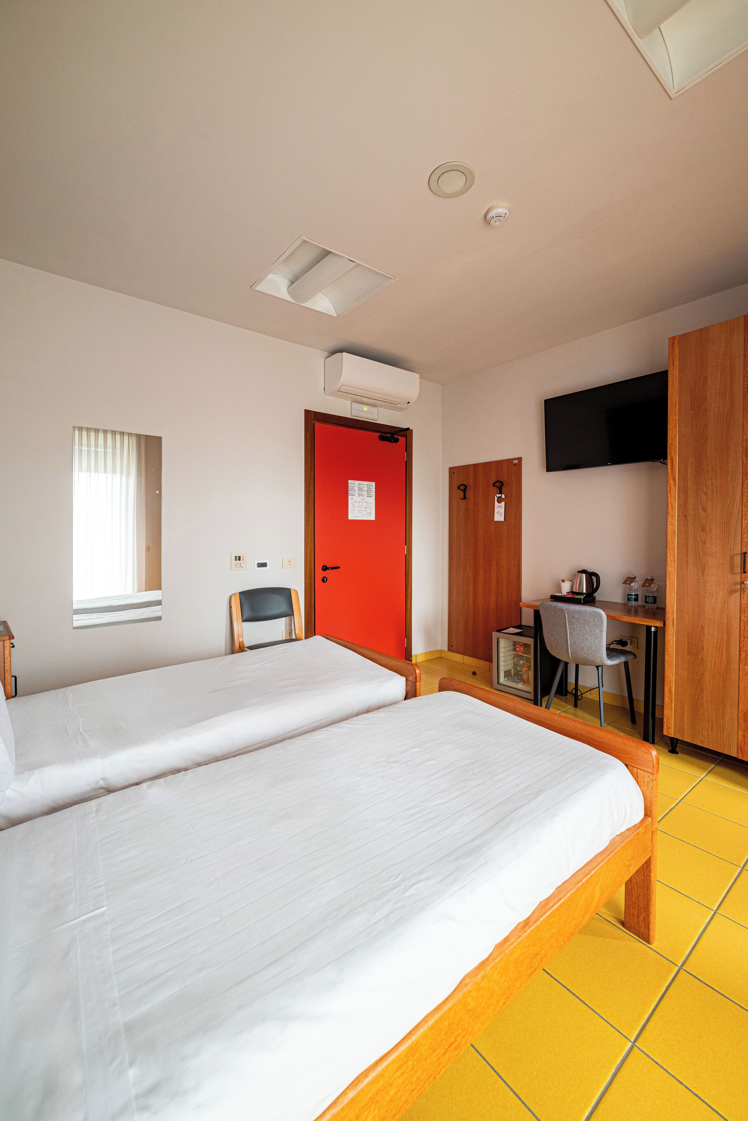 Une chambre d’hôtel avec deux lits, un bureau avec une chaise, une télévision et une porte rouge.