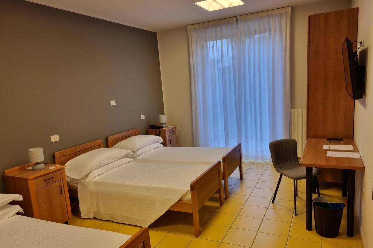 A hotel room with two beds, a desk, a chair, and a television.