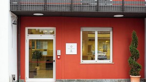 A hotel entrance with a red facade, a glass door, a potted plant, and a sign indicating the hotel name. - Phi Hotel Homy Druento (Druento)