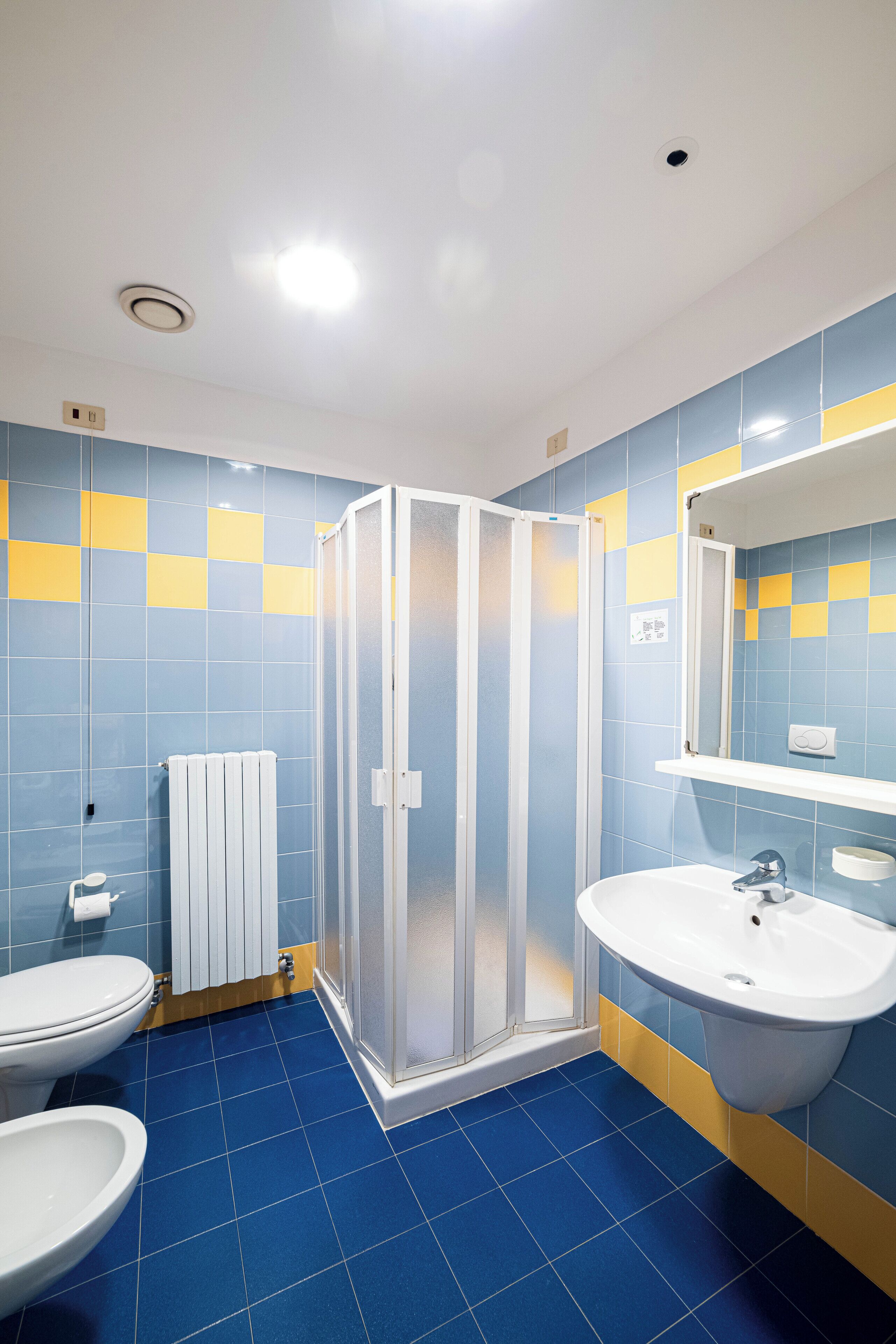 A bathroom with a shower, toilet, and sink, featuring blue and yellow tiles.