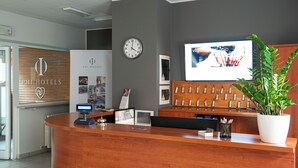 A hotel reception desk with a digital display, a clock, a television, and a plant. - Phi Hotel Homy Druento (Druento)