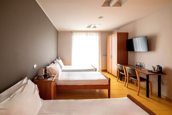 A hotel room with two beds, a desk, a chair, a TV, and a window with curtains.