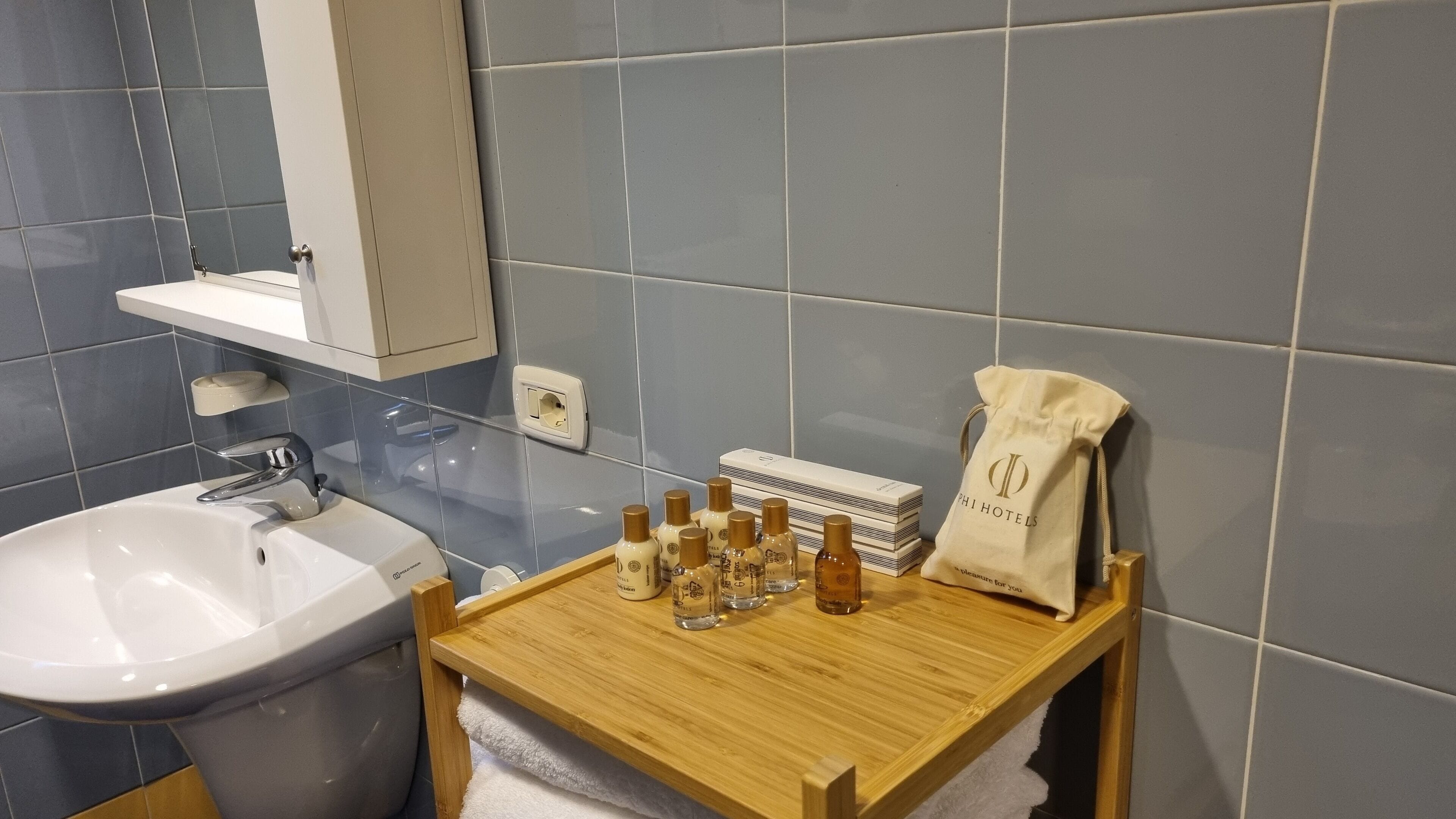 A bathroom with a sink, mirror, and a wooden shelf holding toiletries and a towel.
