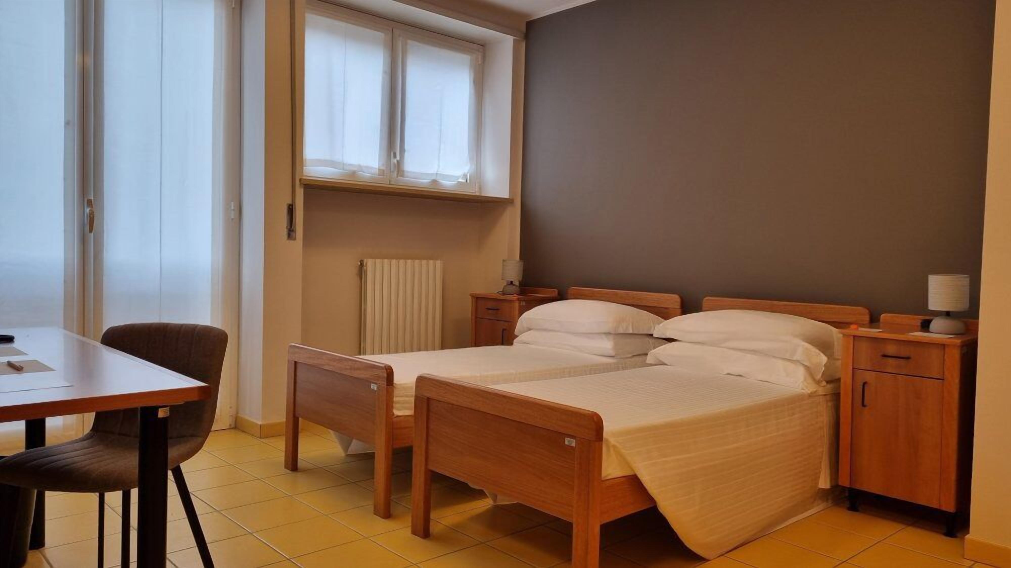 A bedroom with a bed, bedside tables, a chair, a desk, and a window with curtains.