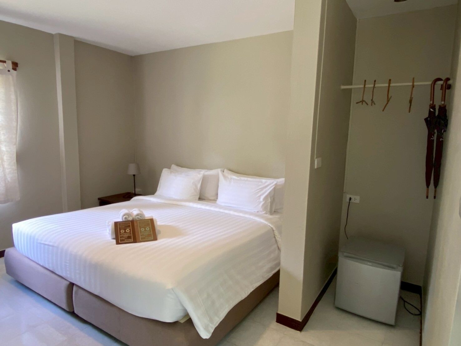 A hotel room with a large bed, a bedside table with a lamp, and a small refrigerator.