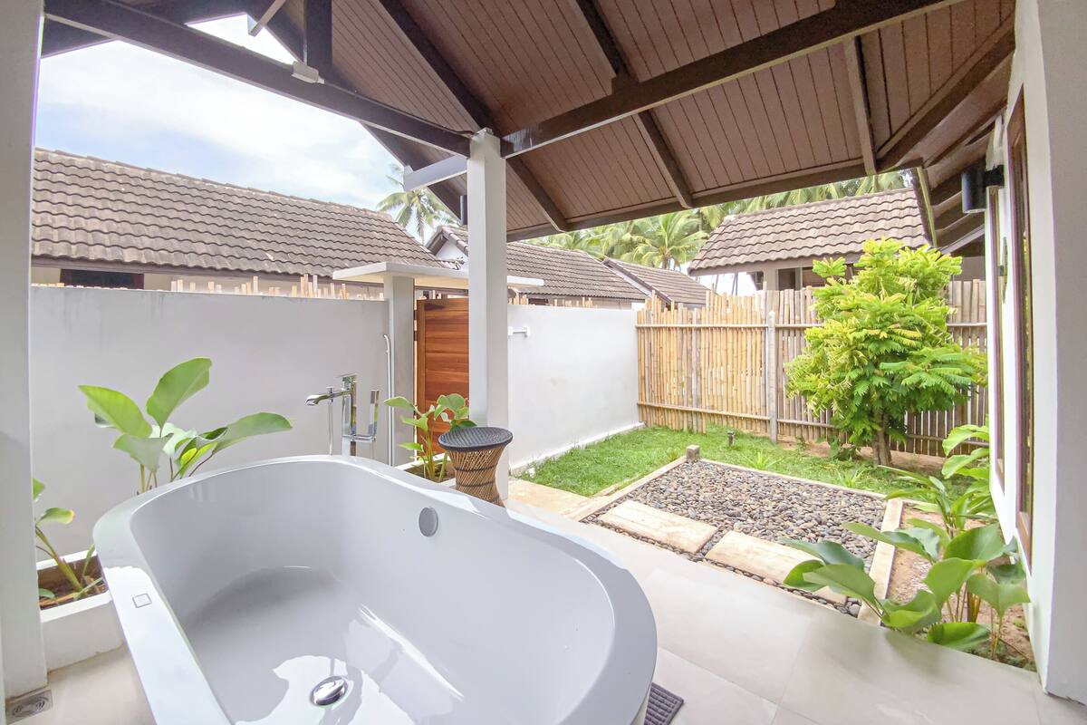 A spa area with a large bathtub, a wooden fence, and a garden.
