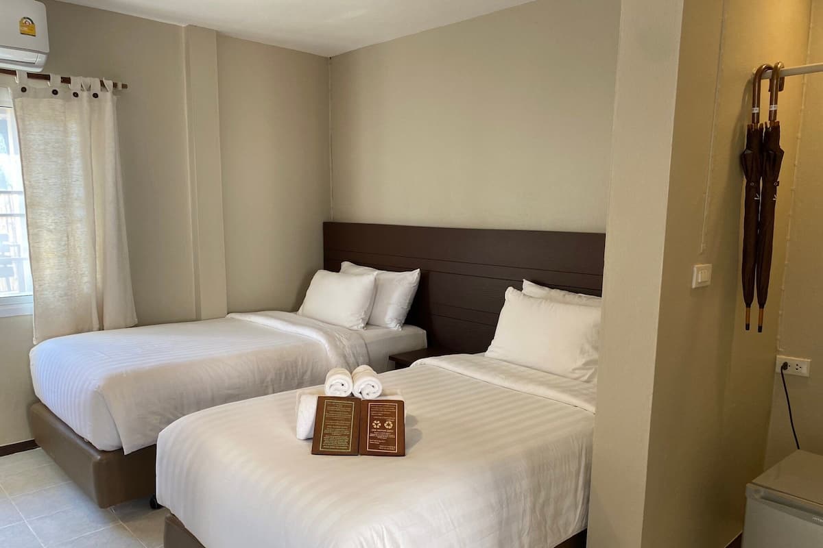 A hotel room with two beds, a small table with a tray of towels, and a minibar.