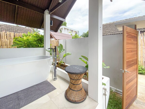 Une salle de bain extérieure moderne avec une baignoire sur pieds, une petite table ronde et une porte en bois.