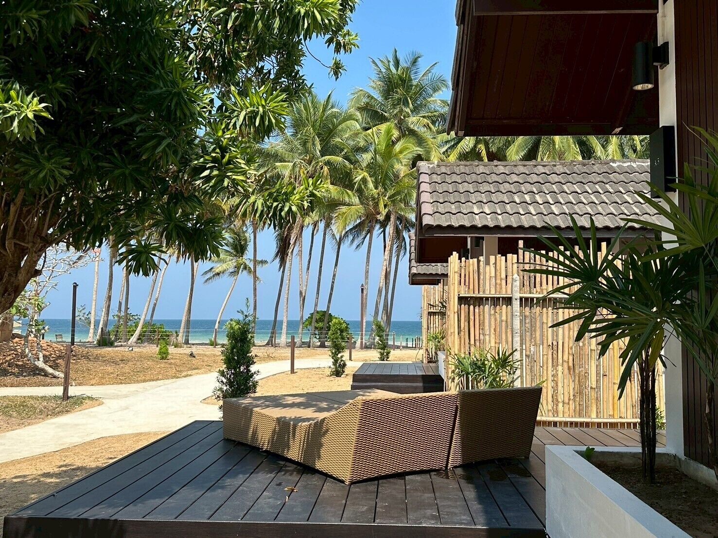 A wooden deck with wicker furniture, palm trees, and a view of the ocean.