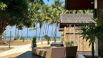 A wooden deck with wicker furniture, palm trees, and a view of the ocean.