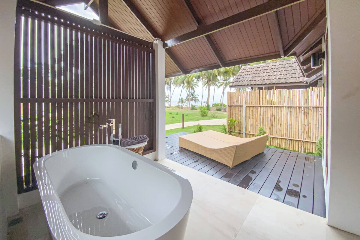 A spa area with a large bathtub, a small seating area, and a view of a wooden fence and greenery.