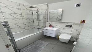 A modern bathroom with a bathtub, a sink, a toilet, and a shower. - Cozy Studio in Brighouse (Brighouse)