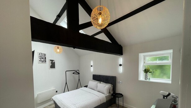 A bedroom with a bed, bedside table, hanging light fixture, radiator, and a window with a view. - Cozy Studio in Brighouse (Brighouse)