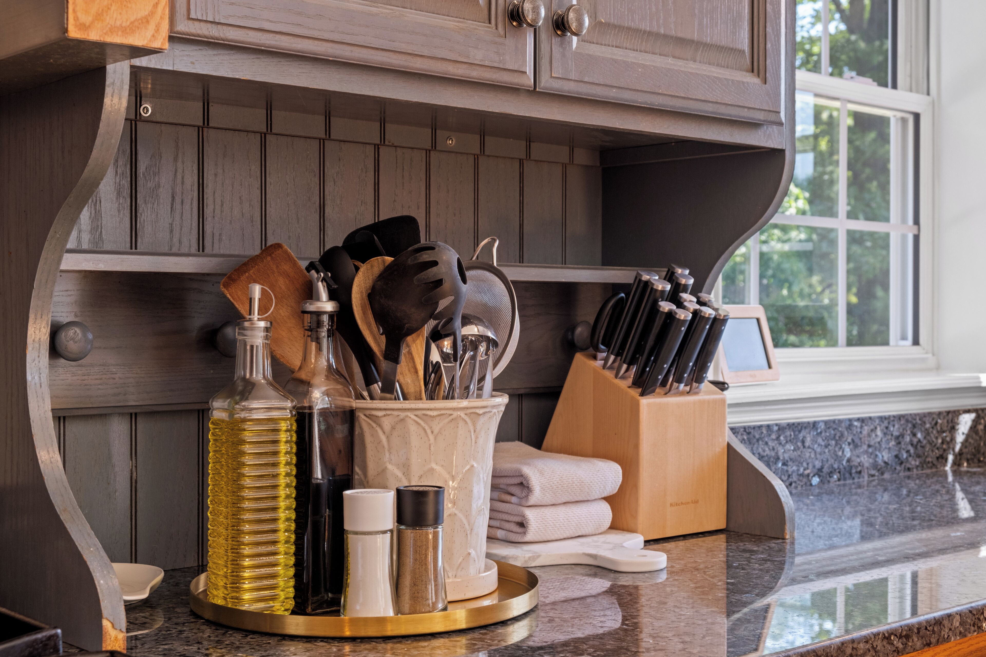 A kitchen counter with a knife block, a spice rack, and a bottle of olive oil.