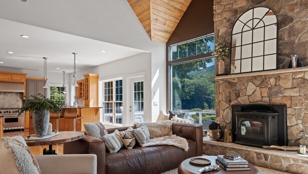 Un amplio salón con chimenea, una pared de piedra y grandes ventanales con vistas al exterior.