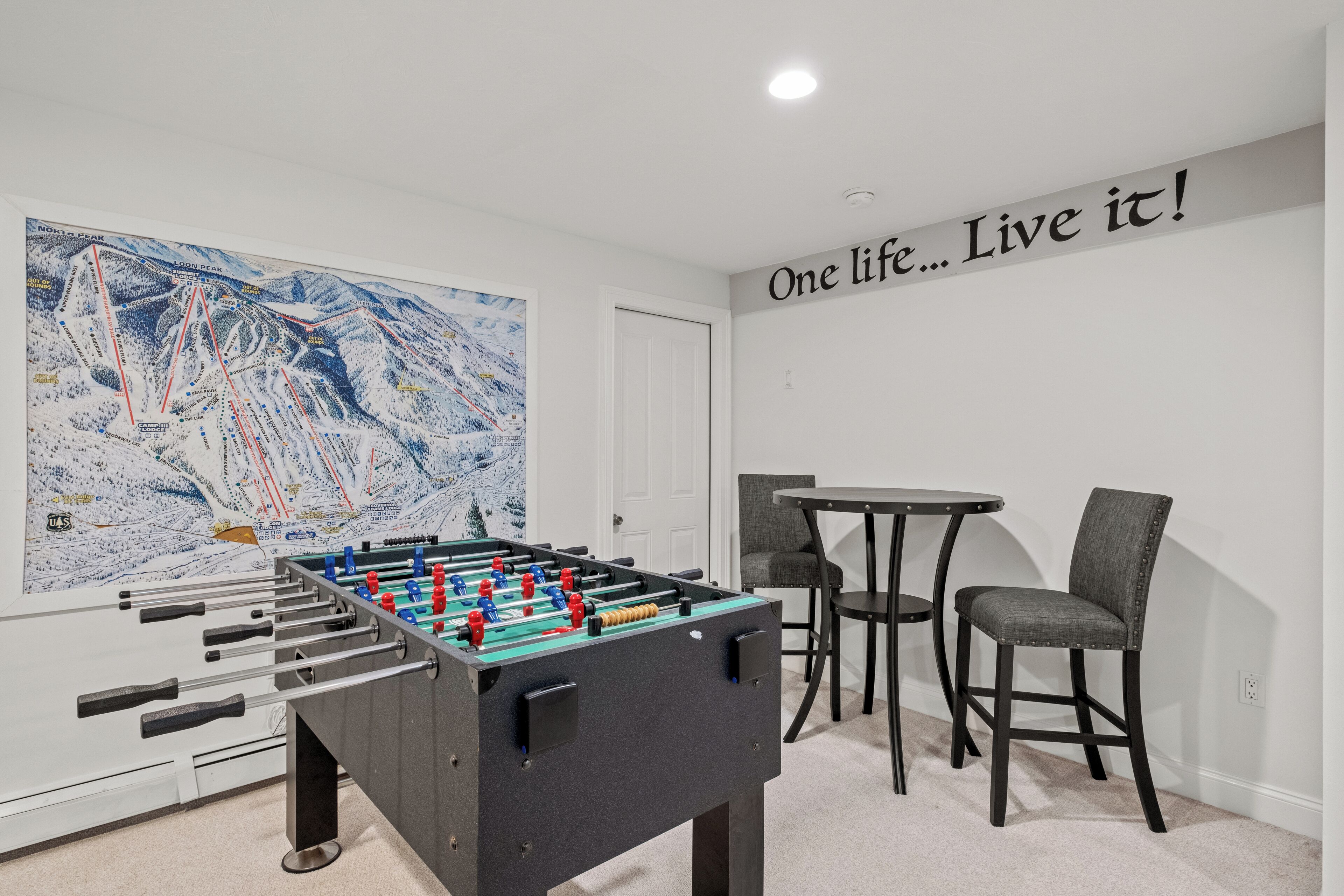 A room with a foosball table, a large abstract painting, a motivational quote on the wall, and a small table with two chairs.