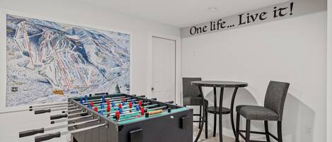 A room with a foosball table, a large abstract painting, a motivational quote on the wall, and a small table with two chairs.
