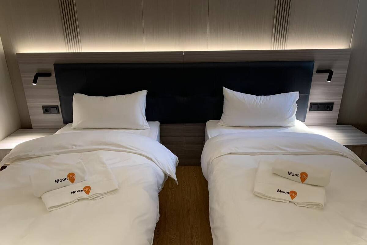 A hotel room with two beds, each with a white bedspread and pillows, and a headboard with built-in lighting.