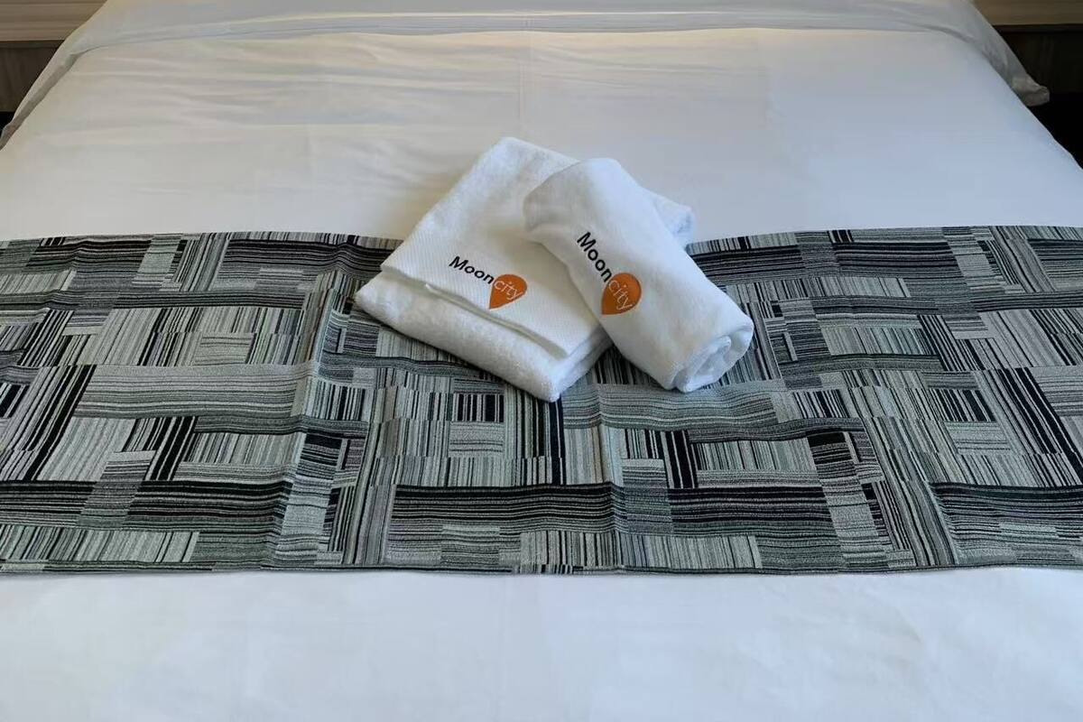 A hotel room with a neatly made bed, a patterned bedspread, and two towels with a logo.