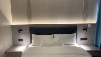 A modern hotel room with a large bed, two bedside tables, and a headboard with integrated lighting.