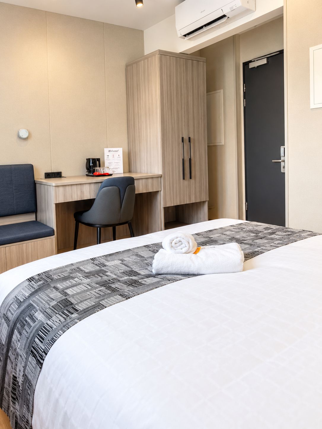Habitación de hotel con cama, escritorio, silla, armario y equipo de aire acondicionado.